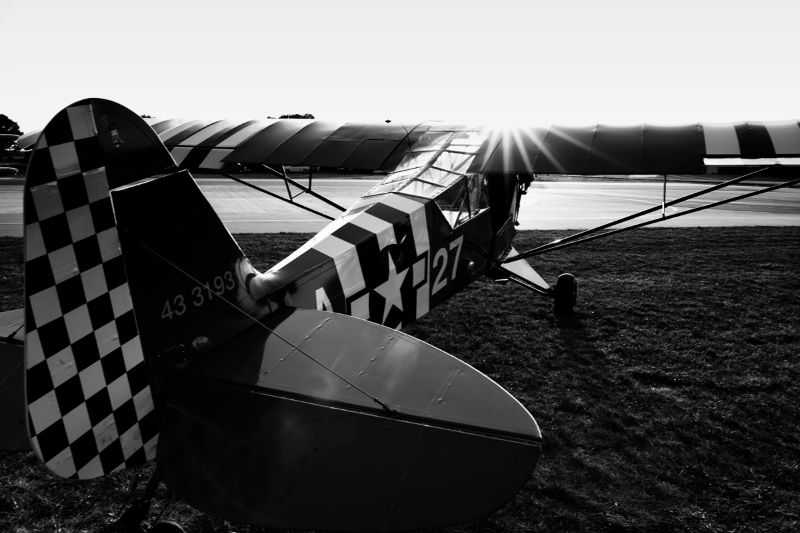 Black & White photo of tail dragger aircraft from the back with sun peeking over the cockpit